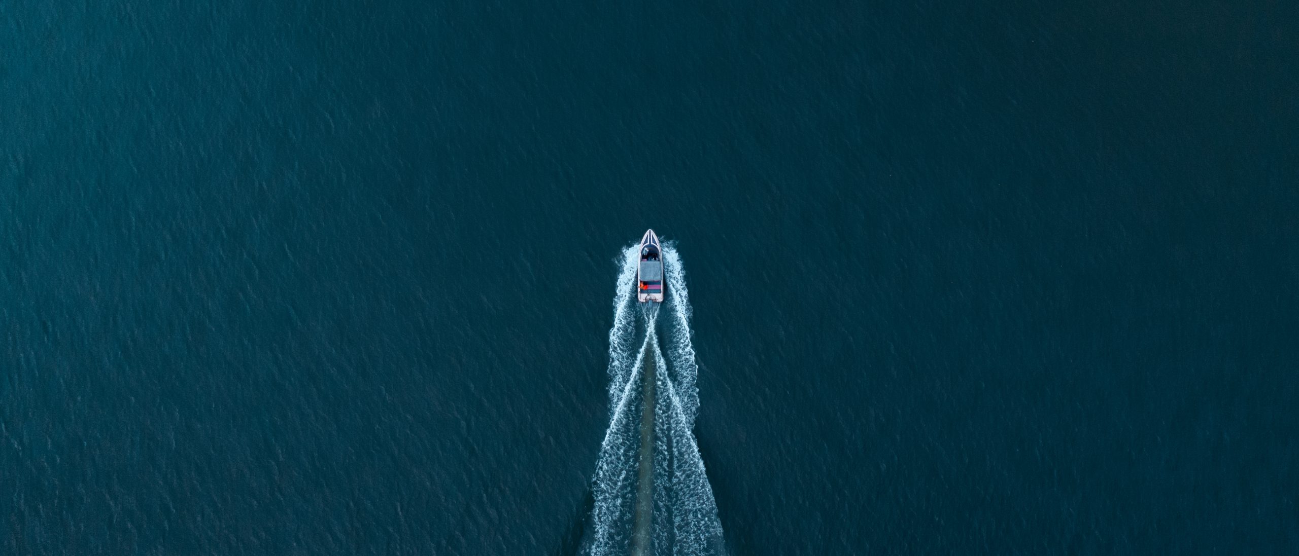 Aerial view of a boat cutting through deep blue water, leaving a symmetrical wake behind.