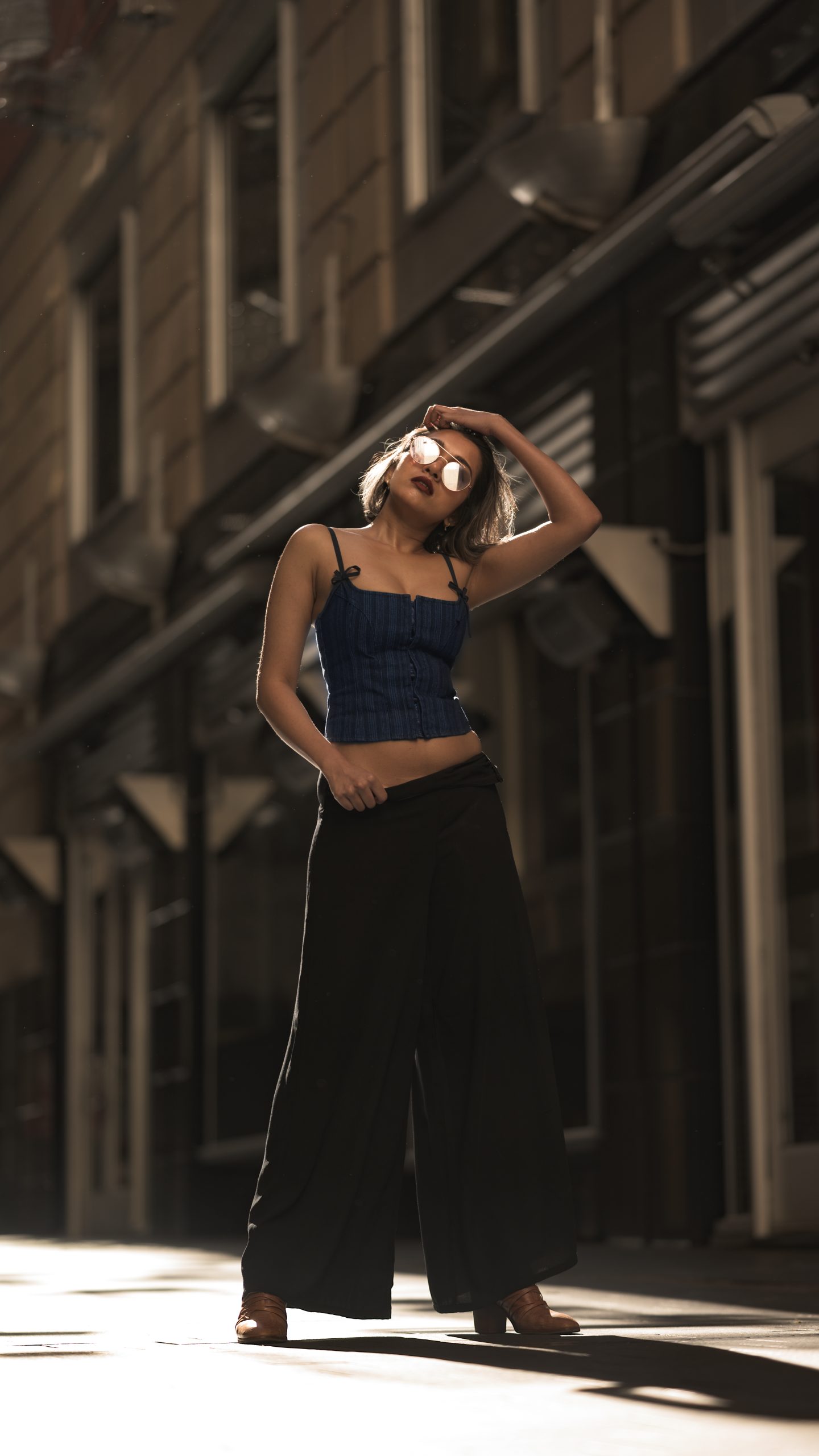 Woman posing confidently in urban sunlight wearing a blue top and black wide-leg pants, captured by Navjyoth Kumar