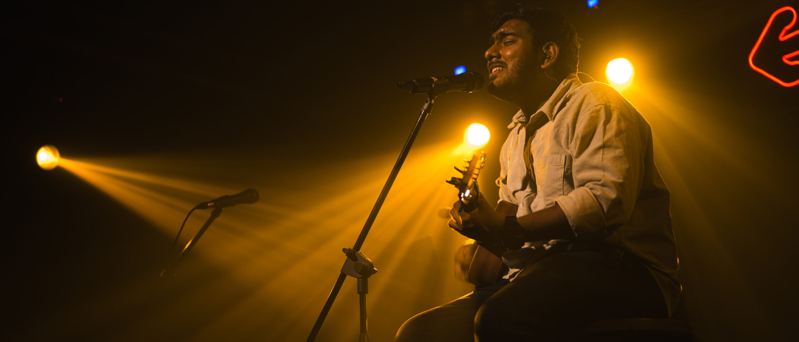 Singer-songwriter performing under dramatic stage lighting with acoustic guitar
