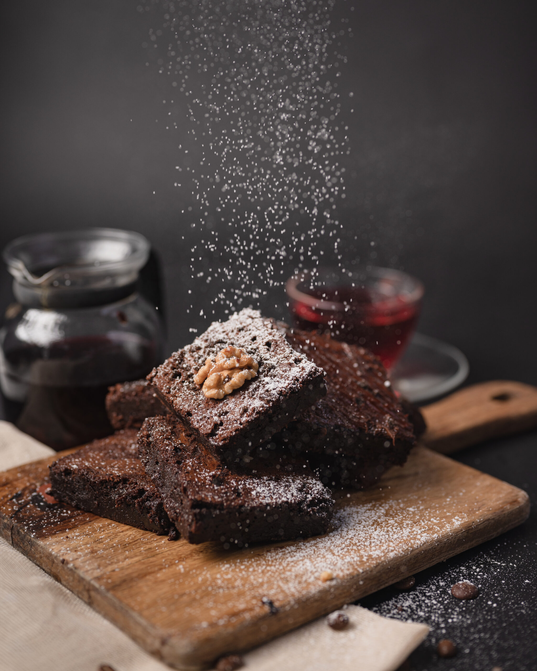 Fudgy brownie stack dusted with falling powdered sugar on wooden board.