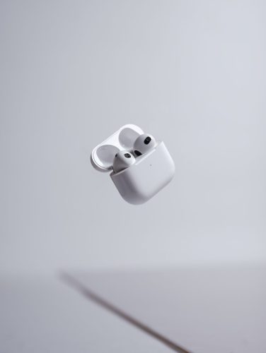 White Apple AirPods floating mid-air with case open on a minimal light grey background.
