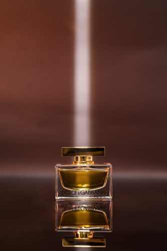 Close-up of Dolce & Gabbana perfume with a diagonal burst of white light over a soft brown surface.