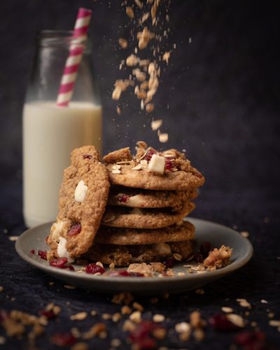 Oat and cranberry cookie stack with crumbs falling against milk backdrop.