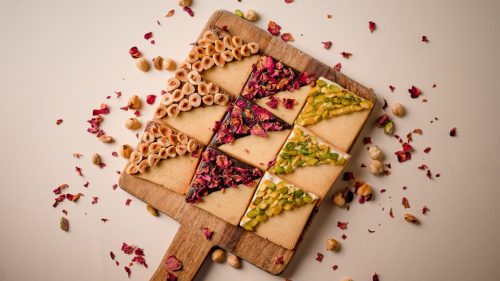 Decorative nut and rose petal dessert triangles arranged on wooden board.