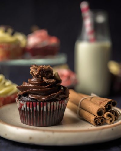 Chocolate cupcake with swirl frosting beside cinnamon sticks and milk bottle.