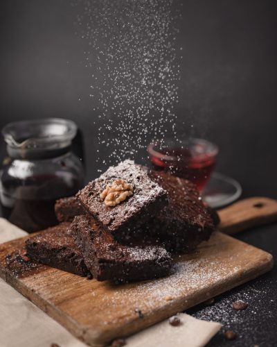 Fudgy brownie stack dusted with falling powdered sugar on wooden board.